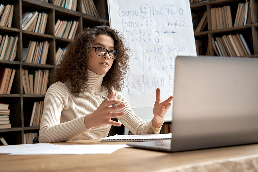 Woman teacher sitting at a desk teaching in front of laptop